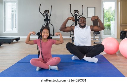 ฺBlack Cornrow Braids girl in sportswear flexing muscles, biceps, triceps with her father on yoga mat. Two yoga ball are placed next to them. Happy family enjoy holiday together in f - Powered by Shutterstock