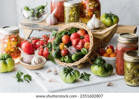 A cornucopia filled with vegetables with vegetable preserves and produce around.