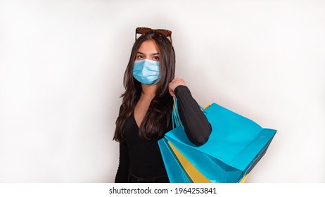 Corona (Covid 19) pandemic. Woman with brown hair goes shopping with medical mask. She holds blue and yellow shopping bags.