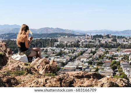 CORONA HEIGHTS PARK, SAN FRANCISCO, CALIFORNIA, USA : A Girl texting on her smartphone while overlooking the city from the top of a hill.