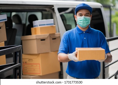 Corona Virus concept, Blue Delivery handsome asian man holding parcel cardboard box and thumbs up with protection mask and medical rubber gloves standing in front of the van