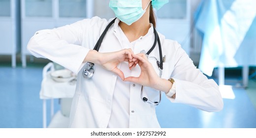 Corona Virus Covid19 Concept. Female European Professional Medic Nurse Wear Face Mask, White Uniform Showing Heart Hands Shape. Medical Love, Care And Safety Symbol. Closeup.