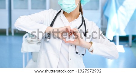 Corona virus Covid19 concept. Female european professional medic nurse wear face mask, white uniform showing heart hands shape. Medical love, care and safety symbol. Closeup.