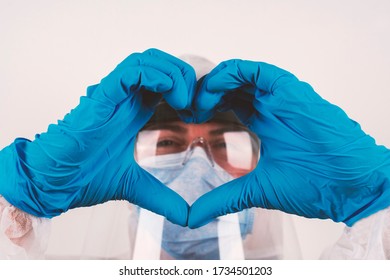 Konzept einer Korona-Virus-Pandemie: Eine Person mit einer hygienisch hygienischen Schutzbrille und blauen Handschuhen schaut durch Finger, die sich zu einer Herzform bilden, um Liebe und Zusammengehörigkeit auszudrücken