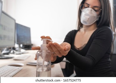 Corona Virus. Woman cleaning her hands at the office. Sick with mask for corona virus. Workplace desk with computer. Woman spraying alcohol gel or antibacterial soap sanitizer.