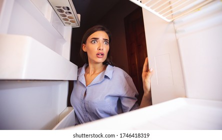 Coronacrisis Concept. Shocked Girl Looking At Her Empty Fridge Shelves In Despair, View From Inside