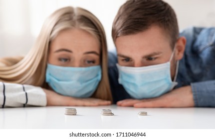 Coronacrisis In Family. Sad Man And Woman In Protective Masks Counting Last Money Savings At Home, Close Up