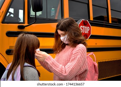 Coronavirus Back To School Reopening: Girls, Children, Students, With Face Masks By School Bus. For Education, Health, Safety, And Environmental Concepts Regarding Coronavirus, Schools, And Facemasks.