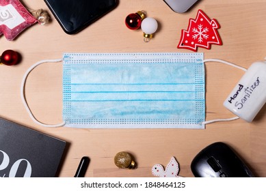 Coronavirus Christmas Holidays Office Concept. Medical Face Mask, 2020 Covid19 Era Christmas Holiday Decorations On Wooden Background. Top View With Office Equipment