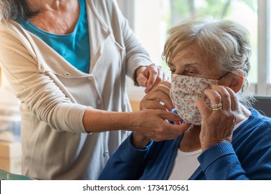 Coronavirus Concept. Isolated Senior Woman And Adult Lady During COVID-19 And Flu Outbreak. Daughter Putting On Face Mask To Her Mother. Quarantine. Stay Home. 