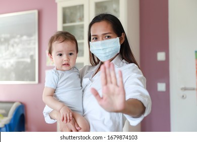 Coronavirus Concept Young Mother Wearing Surgical Face Mask Holding Her Baby And Show Stop Hand During Corona Virus,Covid-19 Pandemic Outbreak. Mixed Race Family Asian-German Mom And Kid Sick ,allergy