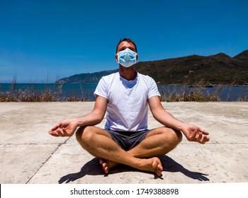 Coronavirus COVID 19. Young beautiful man doing sport performing workouts exercises yoga in the park near sea during quarantine. Active life in surgical sterilizing face mask protection - Powered by Shutterstock