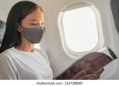 Coronavirus Covid Travel During Pandemic Asian Woman Wearing Face Mask In Cabin Inside Plane During Flight Reading Magazine At Passenger Window Seat. USA Vacation Lifestyle