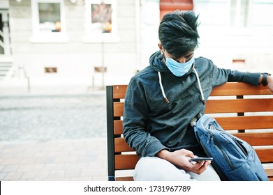 Coronavirus Covid-19 Concept. South Asian Indian Man Wearing Mask For Protect From Corona Virus Sitting On Bench With Mobile Phone.