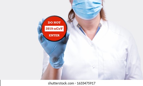 Coronavirus COVID-19 Warning Sign. Female doctor hand holding stop sign with text do not enter coronavirus 2019-nCoV against red background conceptual image.