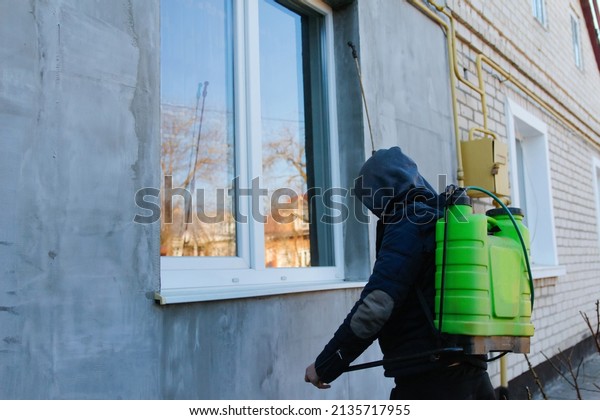 Coronavirus disinfection. People in hood making\
disinfection in house outdoor, copy space, hot steam disinfection.\
Male worker spraying insecticide on window sill outside. Pest\
control. Sanitize.
