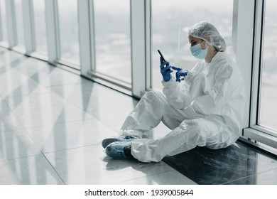 Coronavirus Epidemic Outbreak. Tired Doctor With Respirator In Clean Suit With Mobile Phone