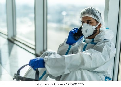 Coronavirus Epidemic Outbreak. Tired Doctor With Respirator In Clean Suit With Mobile Phone