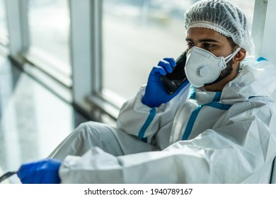 Coronavirus Epidemic Outbreak. Tired Doctor With Respirator In Clean Suit With Mobile Phone