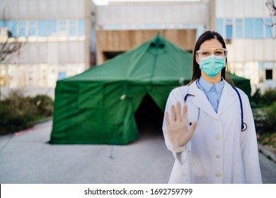 Coronavirus ER Doctor In Front Of Isolation Hospital.Covid-19 Physician With Protective Glasses / Mask Performing Triage For Virus Outbreak Patients.Hand Stop Sign.Quarantined Area.No Entrance Allowed