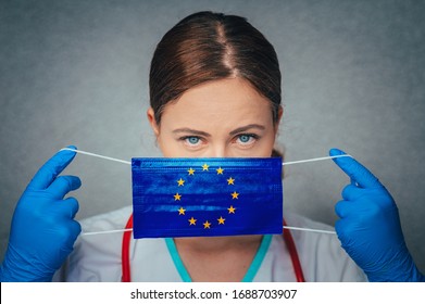 Coronavirus In European Union, Female Doctor Portrait Hold Protect Face Surgical Medical Mask With Europa Union Flag. Illness, Virus Covid-19 In EU, Concept Photo