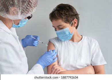 Coronavirus, flu or measles vaccine concept. Medic, doctor, nurse, health practitioner vaccinates teenage boy with vaccine in syringe. She is wearing uniform, hut and gloves. Both have face mask - Powered by Shutterstock