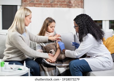 Coronavirus, Flu And Vaccination At Home Concept. Female African Doctor Making Injection Of Vaccine At Home To Stimulating Immunity Of Her Teen Girl Patient At Risk Of Coronavirus Or Flu Infection.