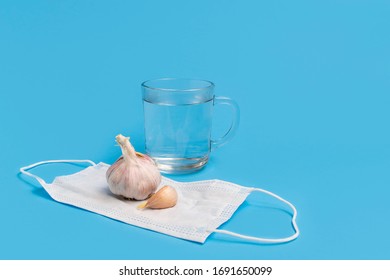 Coronavirus Health Myths Concept, Garlic, Hot Water, Medical Face Mask On Blue Background With Copy Space