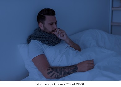 Coronavirus, Influenza Concept. Sick Young Man Coughing, Holding Paper Napkin Near Mouth, Sitting In Bed At Night, Feeling Unwell, Copy Space