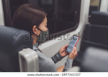 Coronavirus lifestyle bus passenger using mobile phone during commute at night during curfew and lockdown. Woman texting online on contact tracing app while wearing face mask.