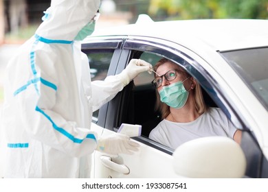 Coronavirus nasal drive-through swab test. Doctor in hazmat suit taking saliva sample for covid-19 diagnostics in a car. Woman driver patient at drive-thru testing station in hospital. Virus outbreak. - Shutterstock ID 1933087541
