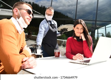 Coronavirus Outbreak Group Of Casual Business People In Outdoor Restaurant Wearing Protective Medical Mask, Business Team Collaborating And Brainstorming Business Ideas  While Working On Laptop