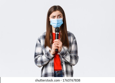 Coronavirus Outbreak, Leisure On Quarantine, Social Distancing And Emotions Concept. Confused Woman In Medical Mask Look Smth Strange, Holding Microphone, Perform, White Background