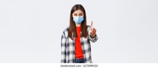 Coronavirus outbreak, leisure on quarantine, social distancing and emotions concept. Serious young woman, elder sister in medical mask shaking finger in stop, prohibition, stay home