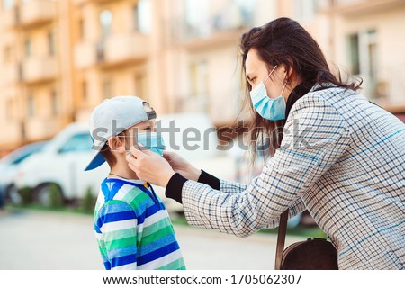 Coronavirus outbreak. Mother puts her son a face protective mask outdoors. Stop the coronavirus spreading. Quarantine. Protective measures. Public crowded place. People prevent infection from virus.