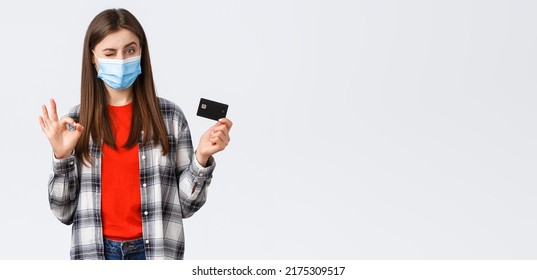 Coronavirus Outbreak, Working From Home, Online Shopping And Contactless Payment Concept. Pleased Young Female Bank Customer In Medical Mask, Show Okay Sign And Credit Card, Wink