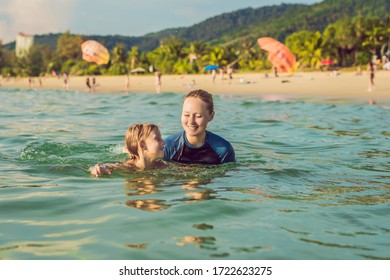 Coronavirus Is Over. Quarantine Weakened. Take Off The Mask. Now You Can Swim. Woman Swimming Instructor For Children Is Teaching A Happy Boy To Swim In The Sea