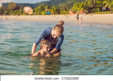 Coronavirus Is Over. Quarantine Weakened. Take Off The Mask. Now You Can Swim. Woman Swimming Instructor For Children Is Teaching A Happy Boy To Swim In The Sea