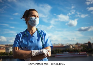coronavirus pandemic. confident modern medical doctor woman in scrubs with stethoscope, medical mask and rubber gloves looking into the distance outside against sky.