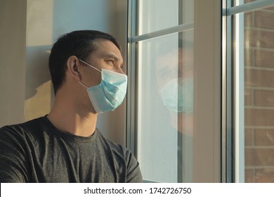 Coronavirus pandemic covid-19 and quarantine concept. Man in a medical mask near window. Man tired of quarantine of Coronavirus. Sick sad man in medical protective face mask looking through window. - Powered by Shutterstock