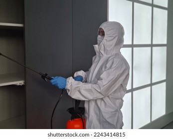 Coronavirus pandemic and disinfectant in protective suit and mask sprays disinfectants in home or office. Protection against COVID-19 disease - Shutterstock ID 2243414815