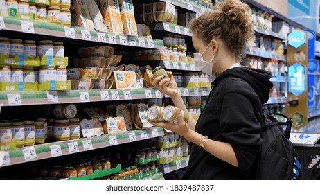 Coronavirus Pandemic. Female Shopper In Face Mask Reading Ingredients Of Baby Pureed Food In Store. Warsaw-Poland-2020.