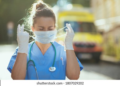 Coronavirus Pandemic. Modern Paramedic Woman In Scrubs With Stethoscope And Medical Mask Outside Near Ambulance.