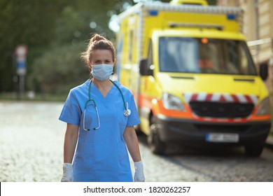 Coronavirus Pandemic. Modern Paramedic Woman In Scrubs With Stethoscope And Medical Mask Outside Near Ambulance.