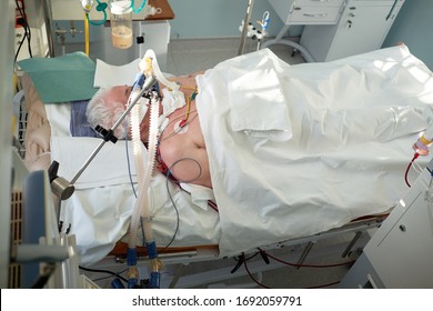 Coronavirus Pandemic. Patient With Coronavirus Pneumonia In Critical State. Intubated Senior Under Ventilator Lying In Coma In Intensive Care Department.