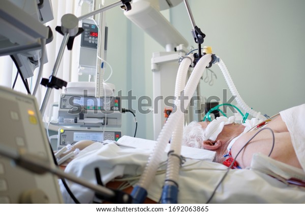Coronavirus pandemic. Patient with\
coronavirus pneumonia in critical state. Intubated senior under\
ventilator lying in coma in intensive care\
department.