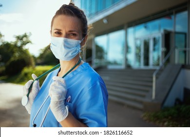 Coronavirus Pandemic. Portrait Of Modern Physician Woman In Scrubs With Stethoscope And Medical Mask Outdoors Near Clinic.