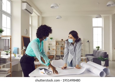 Coronavirus Pandemic, Safety, Return To Workplace After End Of Lockdown And Quarantine. Two Young Creative Designers And Business Women In Face Masks Meeting In Office Studio And Working On Draft Plan