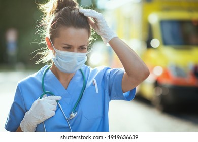 Coronavirus Pandemic. Unhappy Modern Paramedic Woman In Scrubs With Stethoscope And Medical Mask Outside Near Ambulance.