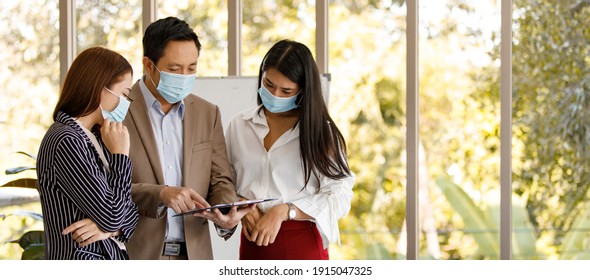 Coronavirus prevention in the office. Group of Asian business people wearing face masks standing reading working discussion in a meeting room. Covid-19 new normal lifestyle concept. - Powered by Shutterstock